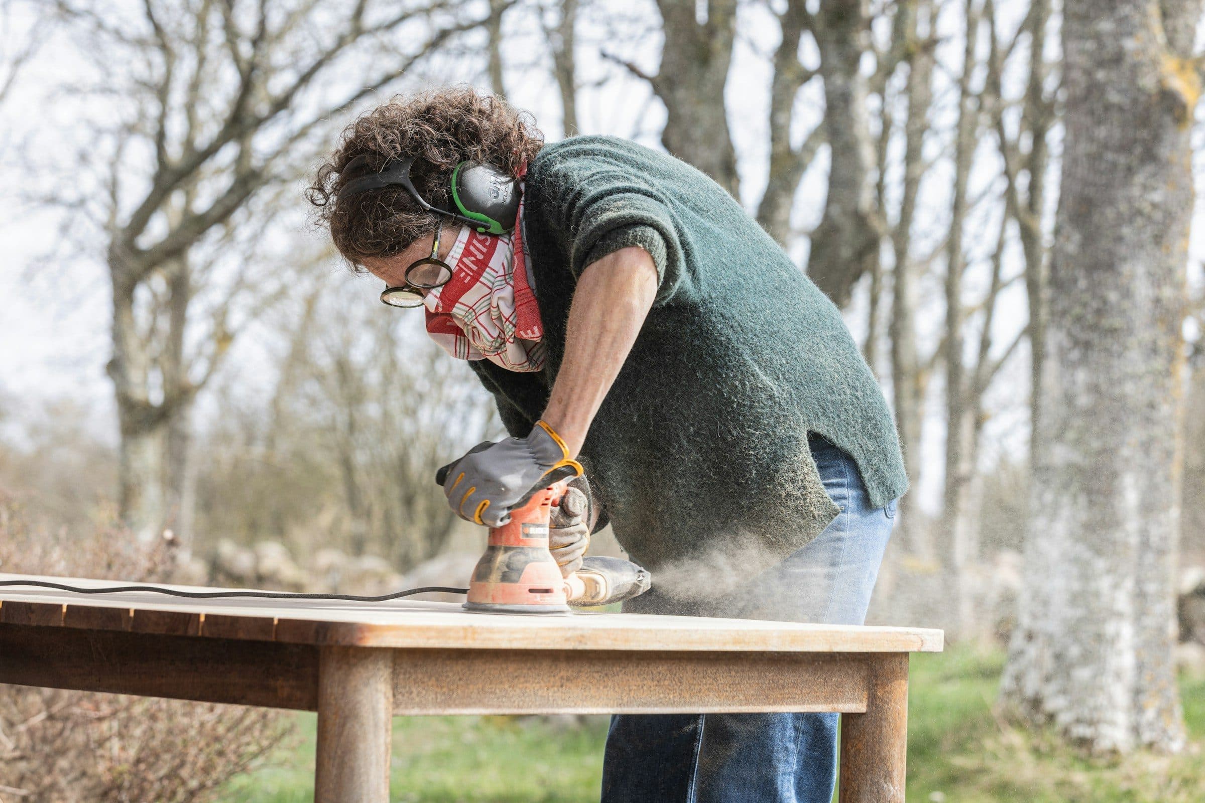 A woman sanding a wooden table outdoors